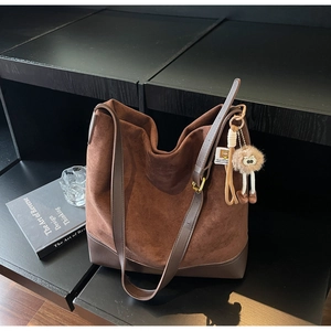Detail of deep brown suede and leather tote bag with stylish plush pendant accessory