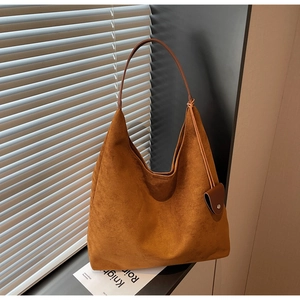 Detail of caramel suede hobo bag with heart charm and matte texture in soft lighting