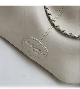 Detail der beigen Ledertasche mit geflochtener Metallkette und geprägtem Mode-Logo-Patch