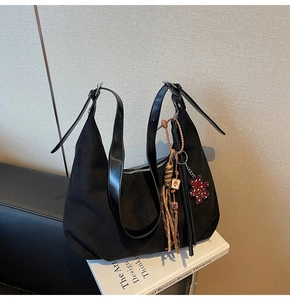 Close-up of black suede hobo bag featuring leopard heart bear charm and woven tassels