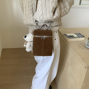 Detailansicht der braunen Wildleder-Box-Umhängetasche mit Bären-Anhänger am Strickpullover