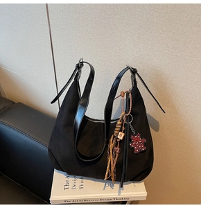 Close-up of black suede dumpling bag with decorative charms and adjustable strap
