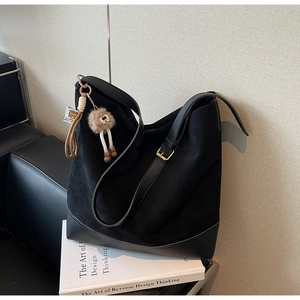 Detail view of black suede tote bag with leather straps and plush charm on books