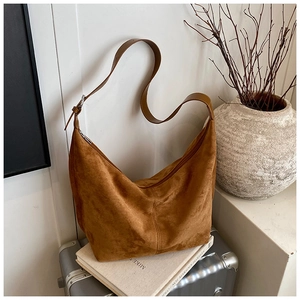 Detail of a dark brown suede hobo bag with adjustable strap on a vintage suitcase