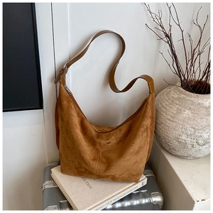 Caramel suede hobo bag on a silver suitcase with a minimalist interior background