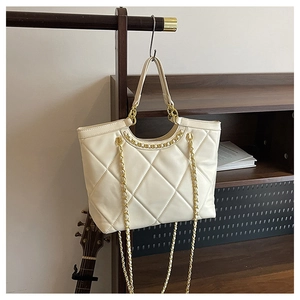 Détail d'un sac cabas beige matelassé avec chaîne suspendu dans un intérieur chaleureux