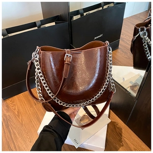 Detail of a brown polished leather bucket bag with silver chain and shoulder strap