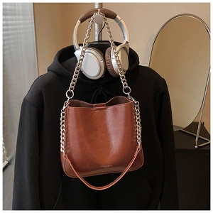 Detail of a brown glossy leather bucket bag with silver metal chain and brand logo