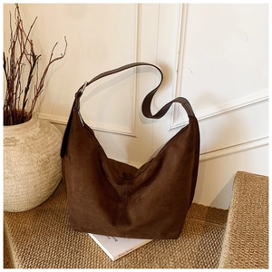 Detail of a dark brown suede tote bag on a textured surface with vintage vase background