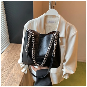 Detail of black glossy leather shoulder bag with bold silver metal chain and long strap