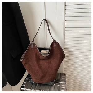 Detail of dark brown suede tote bag with V-shaped opening on a silver suitcase
