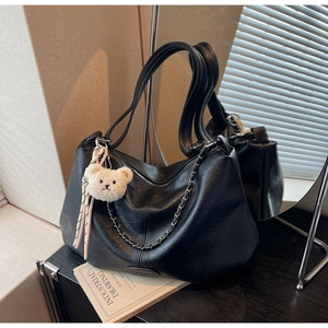 Detail der schwarzen Leder-Tote-Bag mit dicker Metallkette und süßem Teddybär-Anhänger
