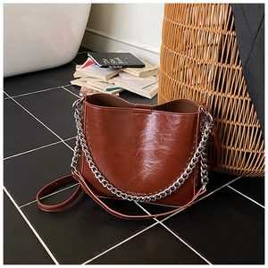 Detail of a caramel glossy leather bucket bag featuring a thick silver metal chain strap