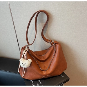 Detailaufnahme der braunen Ledertasche mit verstellbarem Riemen und kleinem Bärenanhänger