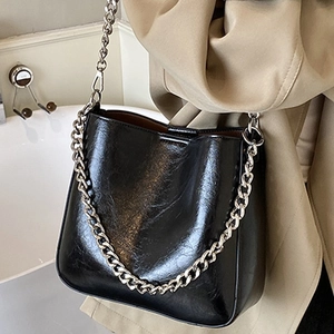 Glossy black leather bucket bag with silver chain strap shown on a khaki trench coat