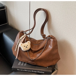 Detailansicht der braunen Ledertasche mit Metallkette und Plüschbär-Anhänger