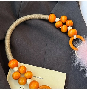 Detalle de cuentas de madera naranjas con pompón rosa y asa de cuerda trenzada