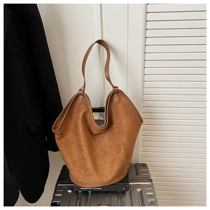 Detailed view of brown suede tote bag placed on a silver metallic suitcase for travel