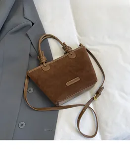 Detailed macro view of a brown suede bucket bag with leather handles and metallic logo plate