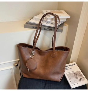 Detail of brown leather tote bag with subtle grain texture and golden logo charm