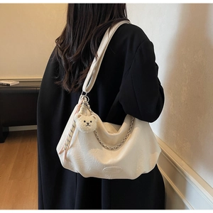 Detailansicht der beigen Hobo-Tasche mit Metallkette, breitem Gurt und Bärenanhänger