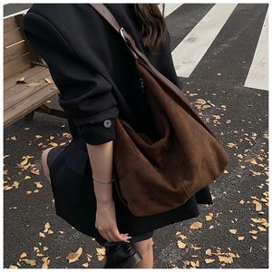Brown suede hobo bag on shoulder against autumn street with fallen ginkgo leaves