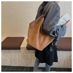 Brown suede tote bag shown on a shoulder in a minimalist lifestyle setting