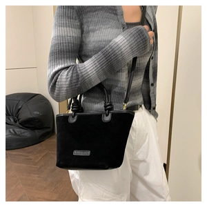 Detail of black suede bucket bag featuring knotted handles and brand metal plaque