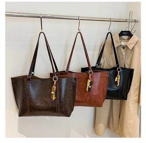 Three retro large-capacity tote bags in brown and black with beaded charms on a rack