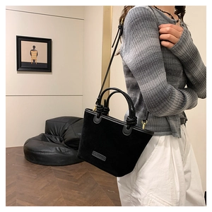 Detail of black faux suede bucket bag with round handles and metal logo plate