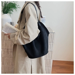 Detail view of a large black matte tote bag with slim straps styled on a model's shoulder