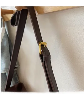 Detail of dark brown leather strap with gold buckle and adjustable stitching on tote bag