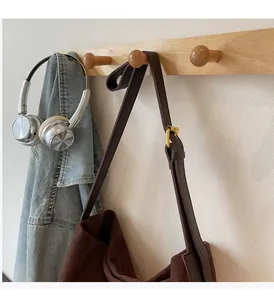 Detail of adjustable golden buckle and long strap on a dark brown suede tote bag