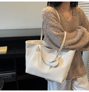 Detail view of cream tote bag with soft leather texture and small coin purse charm