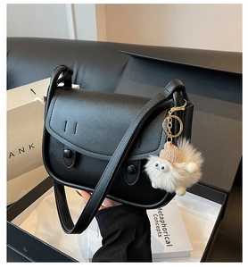 Unboxing view of black leather saddle bag with plush elf charm in premium gift box