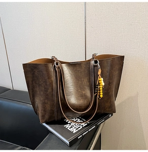 Detailed macro view of dark brown tote bag with vintage texture and beaded charm