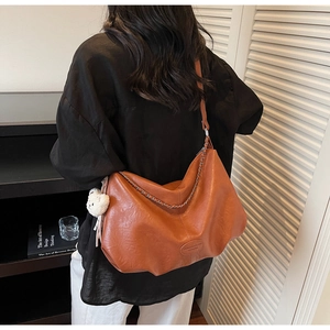 Detailansicht der braunen Ledertasche mit Metallkette und Plüschbär-Anhänger am Model