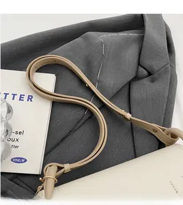 Detail view of cream-colored saddle bag with brown leather strap on gray blazer jacket