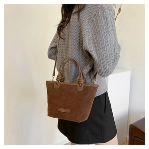 Brown suede bucket bag with top handle and shoulder strap shown on a model