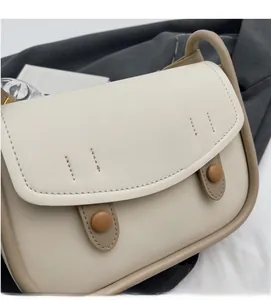 Close-up of beige saddle bag showing contrast stitching and brown button detail