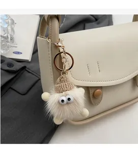 Close-up of a cute beige plush monster bag charm with big eyes and a brown knit hat