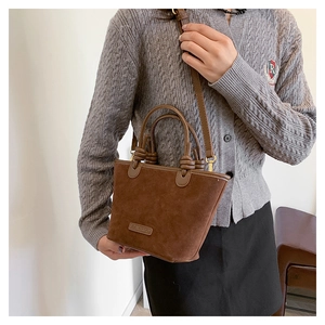 Detail view of the brown suede crossbody bucket bag with elegant knot handle and brand label