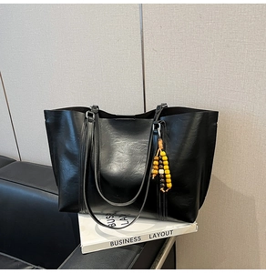 Detail view of black textured leather tote bag with long shoulder straps and wooden bead charm