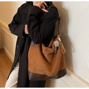 Close-up of brown suede tote bag with leather straps, fringe detail and pompom charm