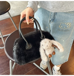 Detail of black faux fur handbag featuring plush rabbit charm and leather handles