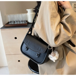 Close-up of black saddle bag with matte leather texture and white plush pendant