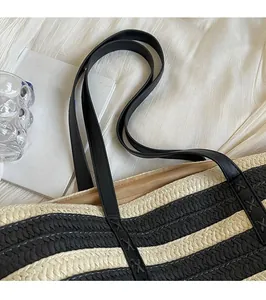 Close-up of woven straw tote bag with black and white stripes and durable leather straps