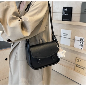 Detail of black matte leather saddle bag with round buttons and a plush sheep charm