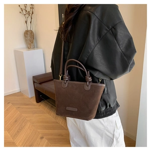 Detailed view of a dark brown suede bucket bag worn cross-body over a black jacket