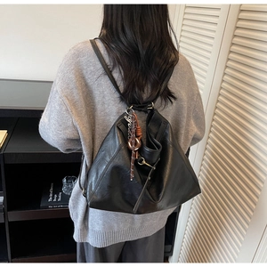 Model wearing a large black leather tote bag with brown woven charm in a modern home setting